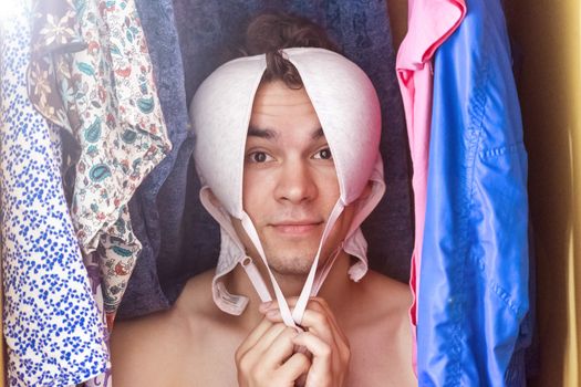 A young man hiding in the closet among women's clothing. Lover in the closet.