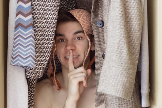 A young man with bra on his head is hiding in the closet