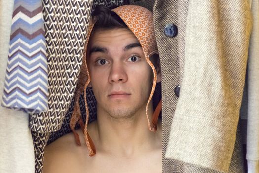 A young man with bra on his head is hiding in the closet