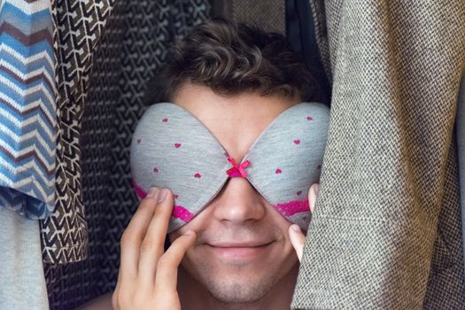 A young man in the closet with a bra on his face.