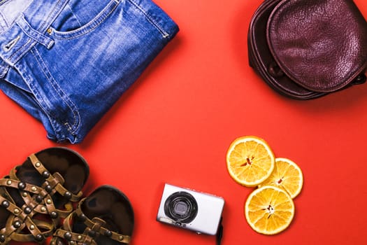 Jeans, sandals, camera, lemon on a red background.