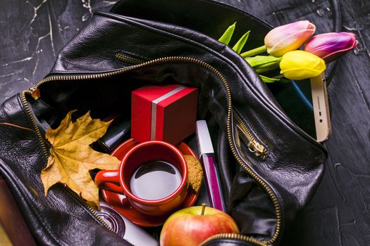 The contents of the female handbag. Flowers, lipstick, camera, coffee, biscuits, beads. Dark background.