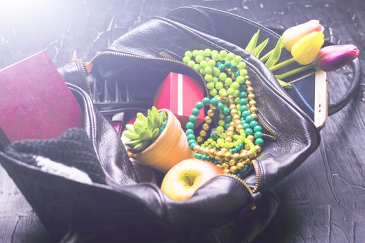 The contents of the female handbag. Flowers, lipstick, camera, coffee, biscuits, beads. Dark background.