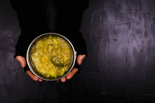 Man in black gloves holding a Cup of soup on a black background.