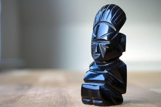 An aztec obsidian ancient statuette on wooden table in sunlight.