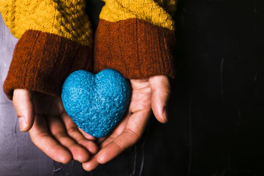 Male hand holds out a blue heart on black background