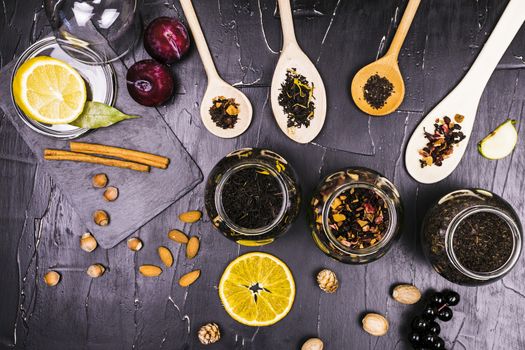 Teas in cans and wooden spoons surrounded by fruit and nut