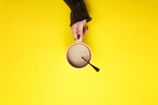 Girl holding a mug of coffee on a yellow background. The concept of a pause, a break.