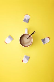 Cup with coffee and tea bags around on a colored background
