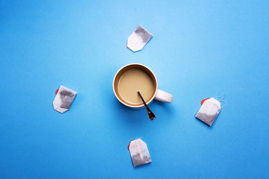 Cup with coffee and tea bags around on a colored background