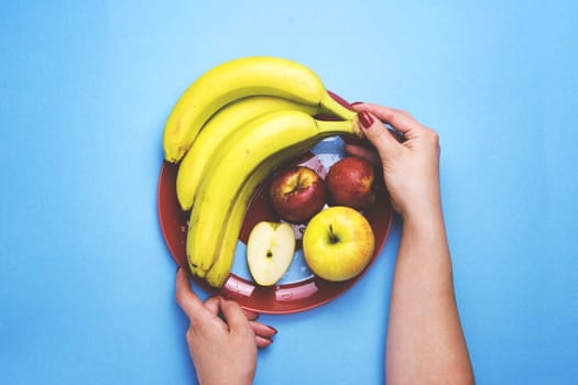 Girl holding a plate of fruit on a color background. The concept of healthy eating, diet.