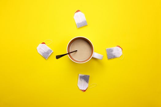 Cup with coffee and tea bags around on a colored background