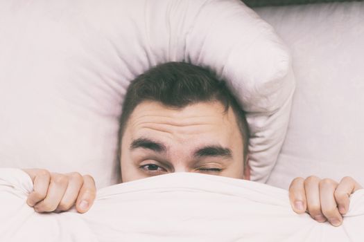 A young man wakes up in the morning under a blanket.