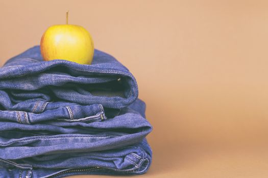 Women's jeans folded in a pile, and on top of the Apple, on a colored background. Made in a vintage performance.
