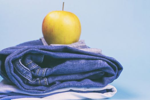 Women's jeans folded in a pile, and on top of the Apple, on a colored background. Made in a vintage performance.