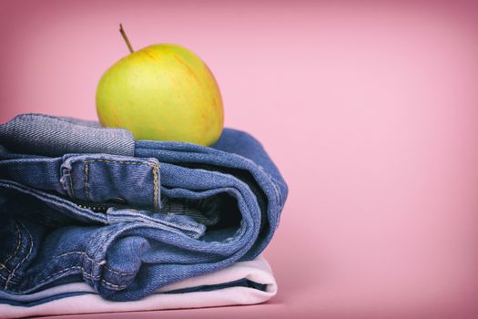 Women's jeans folded in a pile, and on top of the Apple, on a colored background. Made in a vintage performance.