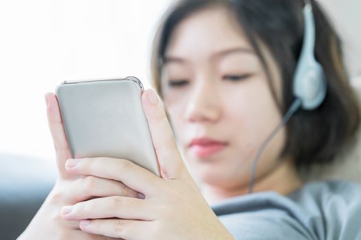 Close up young asian woman short hair listening music from mobile phone on the couch at home