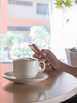 Hand woman using smartphone in coffee shop and a cup of coffee on the table with soft light vintage filter