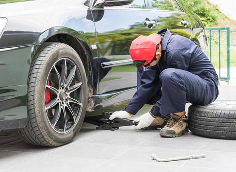 Young mechanic in uniform replacing lug nuts by hand while changing tires on a vehicle