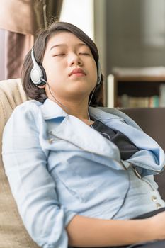 Close up young asian woman short hair listening music from mobile phone by side the window in living room at home