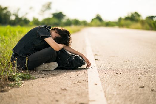 Young asian woman short hair and wearing sunglasses sit with backpack hitchhiking along a road wait for help in country road Thailand