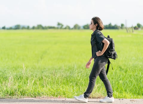 Young asian woman short hair and wearing sunglasses with backpack hitchhiking along a road in countryside Thailand