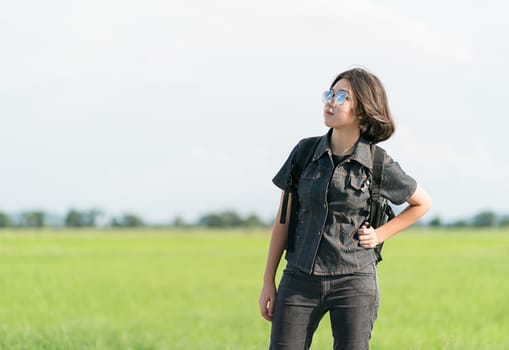 Young asian woman short hair and wearing sunglasses with backpack hitchhiking along a road in countryside Thailand