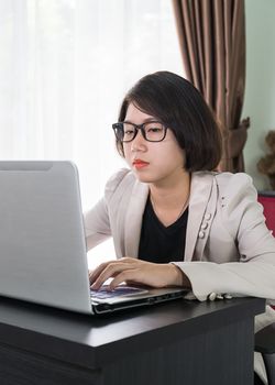 Woman short hair in smart casual wear working on laptop while sitting near window in home office