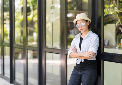 Young women with short hair wearing hat and sunglass standing in front of a glass building