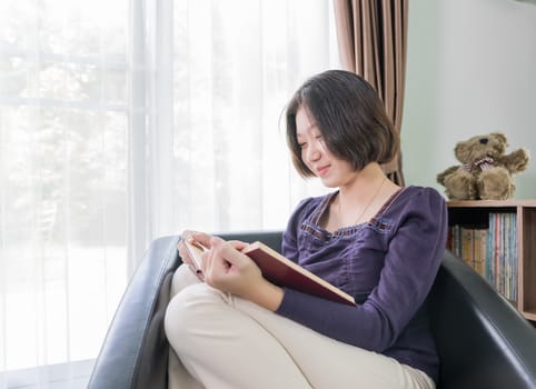 Close up beautiful young asian woman short hair read a book in living room at home