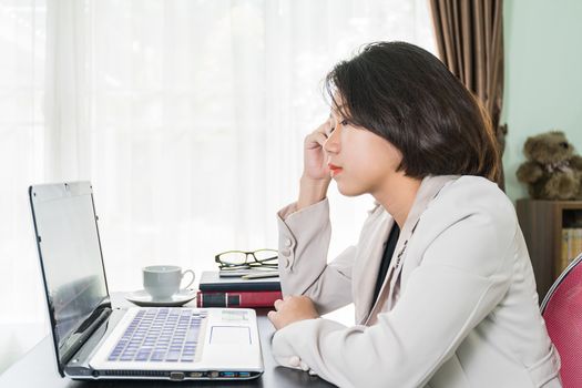 Young asian woman short hair in smart casual wear working on laptop while sitting near window in home office