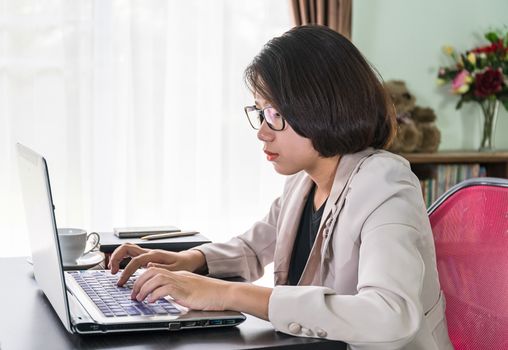 Young asian woman short hair in smart casual wear working on laptop while sitting near window in home office