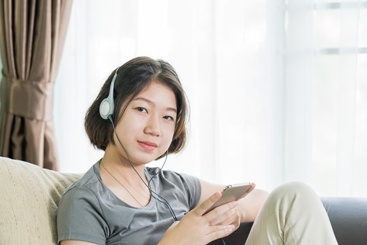 Close up young asian woman short hair listening music from mobile phone on the couch