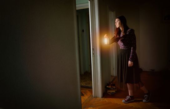 Young girl in black vintage dress with lantern in empty house
