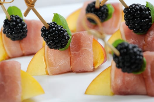 Canape from peach with dried ham and blackberries