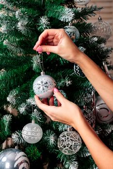 Woman hanging silver Christmas ball on fir tree, holiday concept