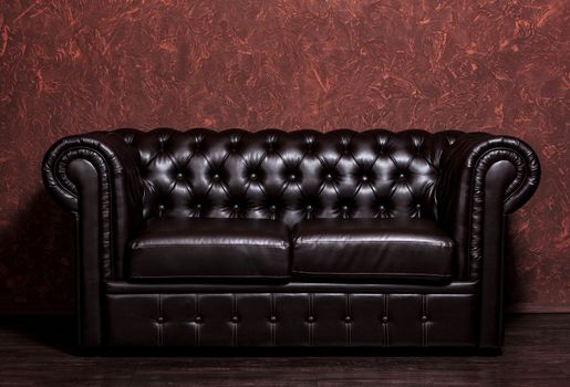 Vintage old dark brown leather sofa with grunge brown wall in the living room