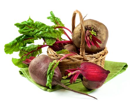 Arrangement of Full Body Fresh Raw Organic Beet Roots and and One Half with Green Beet Tops in Wicker Basket on Napkin isolated on White background
