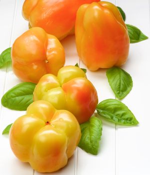 Fresh Crunchy Yellow and Orange Bell Peppers with Green Basil Leafs closeup on White Plank background