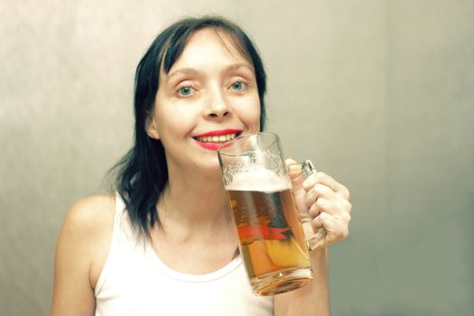 A beautiful woman is drinking beer from a glass beer mug.