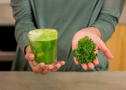 Woman holding a glass of green juice. Preparing a detox juice. 