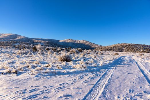 Winter sunny blue sky landscape with car tracks and snowy mountain