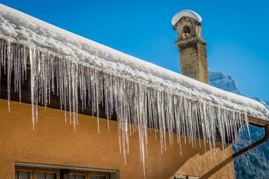 Ice stalactites on a roof brightly shining in the morning sun in winter