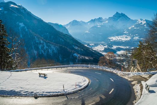 Hairpin bend in the mountains of Switzerland with snow and a bench