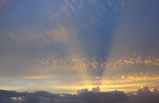 Sun rays from behind clouds stretch their golden light across the sky above