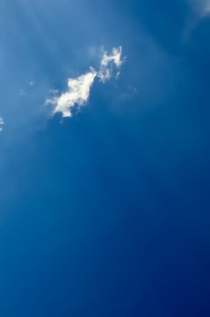 vaste blue sky with sunrays across little fluffy cloud, vertical