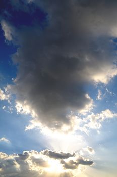 vaste blue sky with stormy clouds and sunrays at twilight, vertical