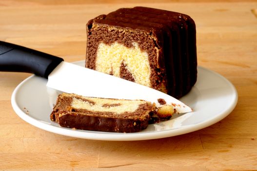 Cutting a slice of delicious chocolate marbled cake, with a white ceramic knife