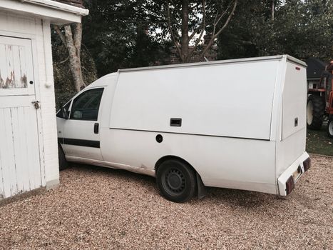 Long white food truck staying in the garden near white garage.