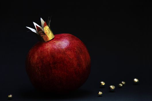 large red pomegranatre or garnet with a golden crown on a dark background. photo